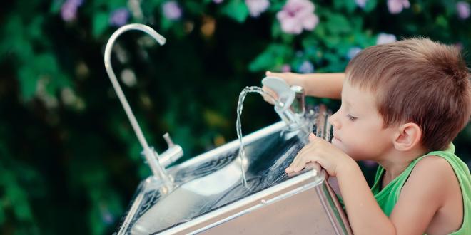 a young boy drinking from a water bubbler fountain in the park